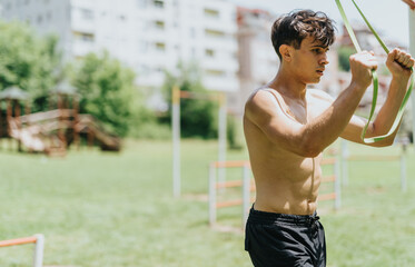 Fit young man working out with resistance bands in outdoor park setting, demonstrating strength and...
