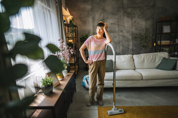 Fototapeta premium Exhausted, tired mature japanese woman stand with a vacuum cleaner