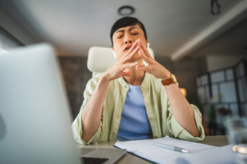 Exhausted, tired mature japanese woman with earphones work from home