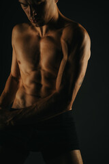 Fototapeta premium Athletic man displaying well-defined abs and arm muscles, highlighting a fit physique against a dark backdrop.