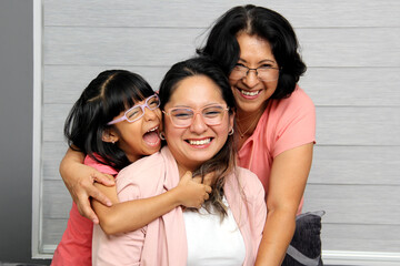 Brunette Latina grandmother, mom and daughter with glasses show their love and support to celebrate...