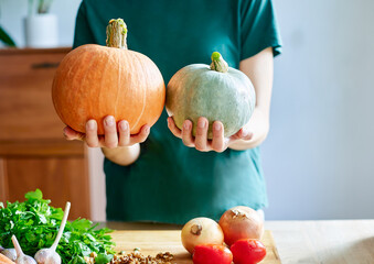 Woman holding two large ripe pumpkins in her hands, cooking food in her home kitchen. Large ripe pumpkins in your hands. Autumn harvest, Halloween, Thanksgiving. Autumn Harvest