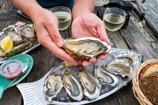 Eating of fresh live oysters with citron at farm cafe in oyster-farming village, Arcachon bay, Gujan-Mestras port, Bordeaux, France in sunny day, huge oyster