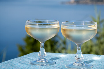 Cold sparkling wine, cava or champagne in two coupe glasses on table with blue sea water view