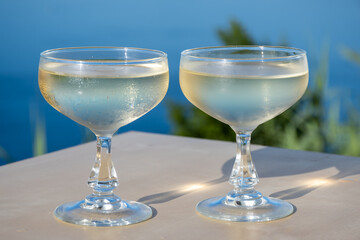 Cold sparkling wine, cava or champagne in two coupe glasses on table with blue sea water view