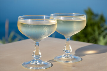 Cold sparkling wine, cava or champagne in two coupe glasses on table with blue sea water view