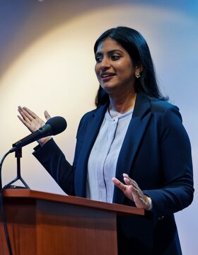 Confident businesswoman delivering an inspiring speech at a podium, exuding leadership and charisma. Ideal for themes of public speaking, empowerment, and professional leadership.
