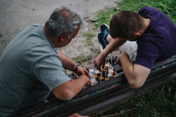 Two men are engaged in an intense outdoor chess game on a park bench, showcasing strategic thinking...