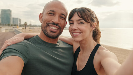 Obraz premium A multi-ethnic man and woman takes a photo of themselves, greeting followers and laughing, takes a selfie for content. Male and female athletes by the sea using phone camera