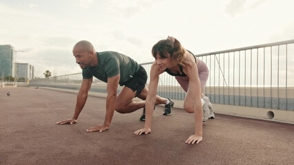 Close-up of multiethnic sportsman and sportswoman doing mountain climber exercise, sporty bodybuilders doing running dynamic plank, loss weight cardio street workout