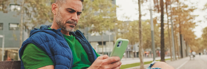 Mature man tourist wearing casual clothes sitting on bench scrolling smartphone