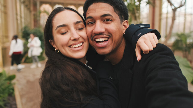 Happy couple taking selfie with smartphone in greenhouse with lush plants