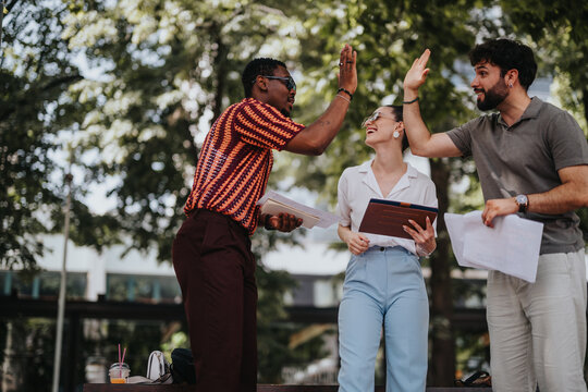 Diverse colleagues outdoor high five celebrating success. Business meeting teamwork concept with happy team members.