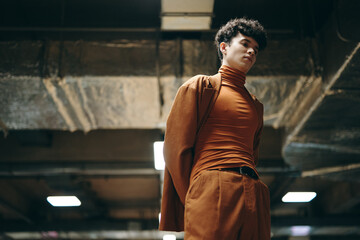 Young man in stylish brown outfit standing in an underground parking garage with industrial background