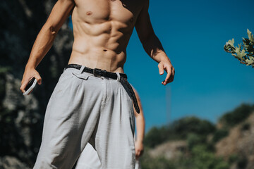 Shirtless man outdoors showcasing his fit and defined upper body while holding a smart phone under...