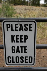 "Please Keep Gate Closed" sign on metal gate to public land hiking trail in area with cattle grazing.