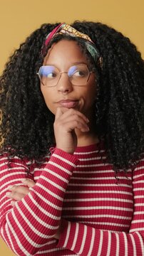 Confused woman cannot make choice on yellow background in the studio
