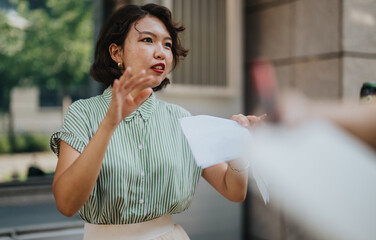 Young woman giving a passionate speech outdoors while holding papers in her hand, looks determined...