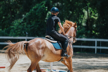 A young rider in a helmet and black attire practicing horse riding at an outdoor arena with green...