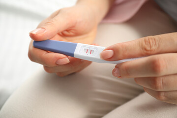 Woman holding positive pregnancy test indoors, closeup view