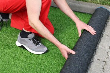 Man in uniform installing artificial turf outdoors, closeup