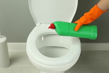 Woman cleaning toilet with detergent in bathroom, closeup