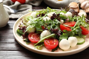 Tasty salad with arugula, lettuce, mozzarella cheese and vegetables on wooden table, closeup