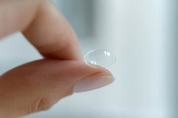 A close-up image of a person holding a clear contact lens delicately between their fingers, showcasing eye care and vision.