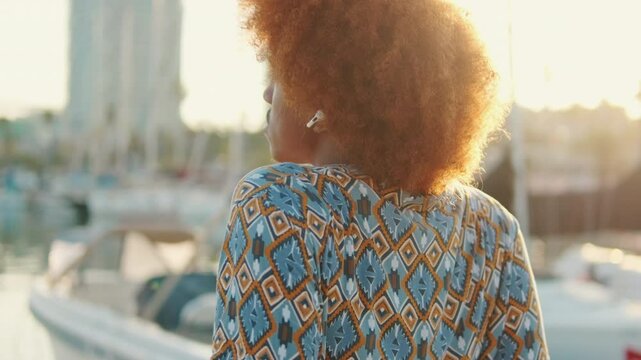 A guy with curly hair and headphones on siiting yacht marina by the sea. The camera rotates around 