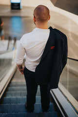 A rear view of a businessman in a white shirt and jacket descending an escalator in a modern building during the daytime.