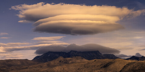 Lenticular clouds over a mountain range during sunset in a vast, tranquil desert landscape