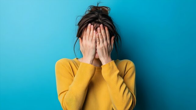 Portrait of a frustrated individual with a hand covering their face in a facepalm gesture set against an isolated background conveying a sense of stress problem or issue