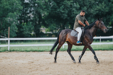 Man enjoying horseback riding in a sandy arena surrounded by greenery, showcasing leisure activity and nature.