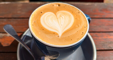 Close up of delicious golden flat white coffee with love heart shaped latte art in smooth silky...