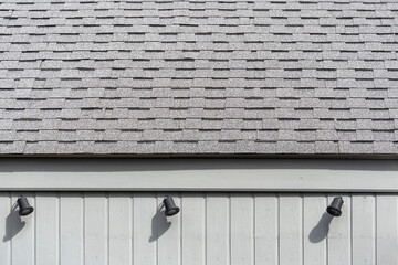 Modern asphalt tiles on the roof with black spotlight and wooden grey color building.