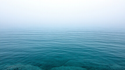 Fototapeta premium Serene lake shrouded in mist at dawn, reflecting the calm water and distant horizon. Ideal for themes of tranquility, introspection, and natural beauty