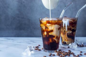 iced coffee with milk poured in glass with glass straw on marble floor