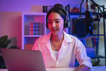 Cheerful beautiful Asian woman wearing headphones and using laptop record podcast. Content creator concept.