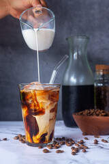 iced coffee with milk poured in glass with glass straw on marble floor