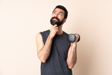 Caucasian sport man with beard making weightlifting over isolated background and looking up