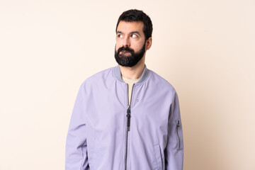 Caucasian man with beard wearing a jacket over isolated background having doubts while looking up