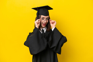 Young university graduate Ukrainian woman isolated on yellow background with glasses and surprised