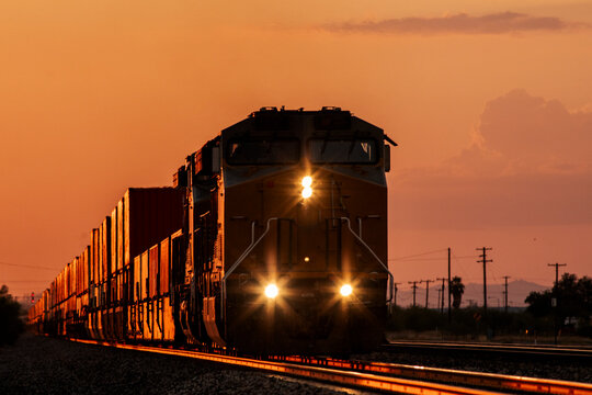 A train approaches closely silhouetted by amber sunset