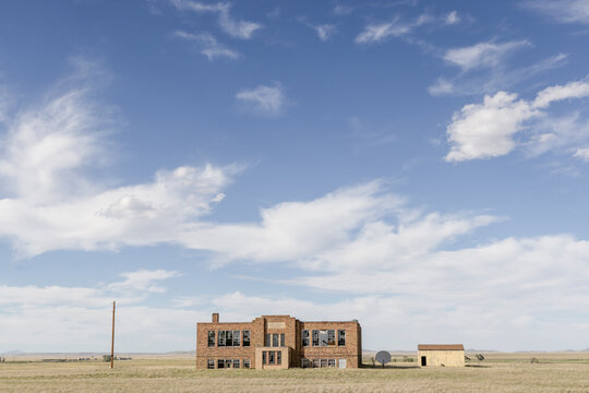 An abandoned school building standing in a field wide view