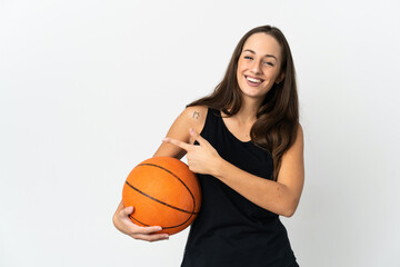 Young hispanic woman over isolated white background playing basketball and pointing to the lateral