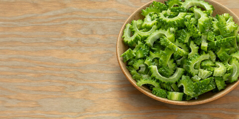 Bitter melon chunks prepared to cook or fry in a bowl. Wooden background with space for text.