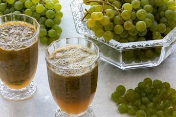 Freshly blended thick grape drink with seeds and pieces of skin in glasses. On the side bunches of...