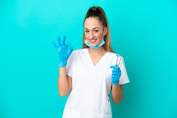 Dentist caucasian woman holding tools isolated on blue background showing ok sign with fingers