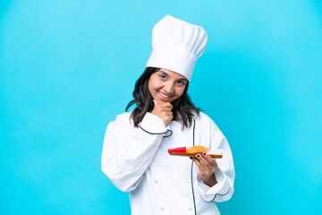 Young hispanic chef woman holding sashimi isolated on blue background happy and smiling