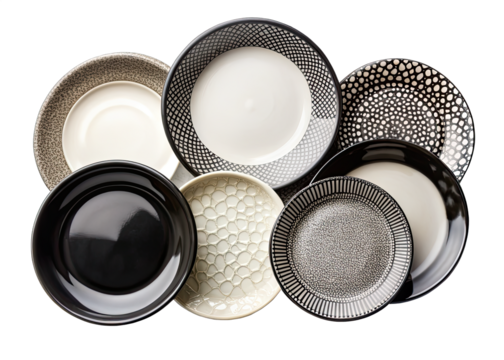 A collection of seven black and white ceramic plates with different geometric patterns are arranged in a circular shape on a white background. The plates are all different sizes and shapes, and they a
